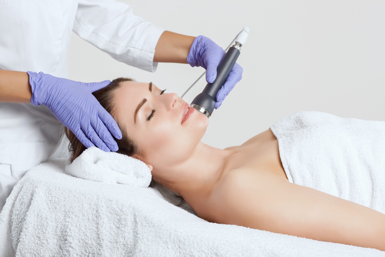 The cosmetologist makes the procedure an ultrasonic treatment of the facial skin of a beautiful, young woman
